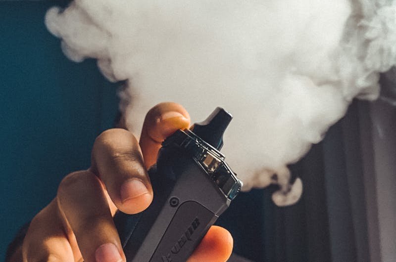 Hand holding a vaping device with a large cloud of smoke, indoors.