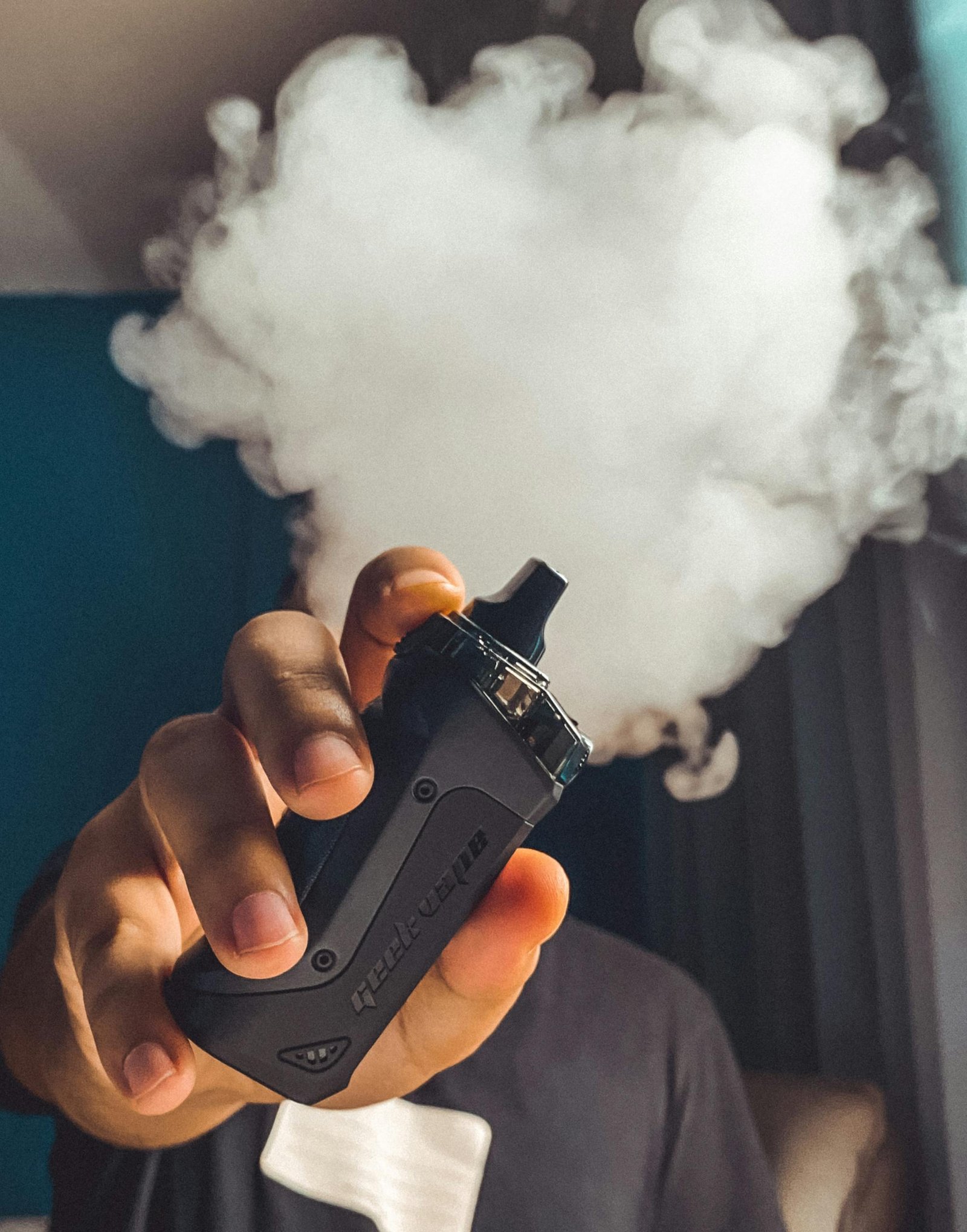 Hand holding a vaping device with a large cloud of smoke, indoors.